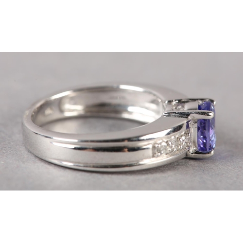 174 - A TANZANITE AND DIAMOND RING in 18ct white gold by Iliana, claw set to the centre with an oval facet... 