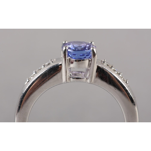 174 - A TANZANITE AND DIAMOND RING in 18ct white gold by Iliana, claw set to the centre with an oval facet... 