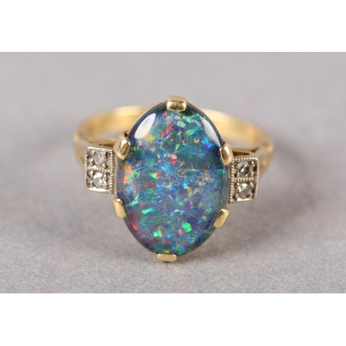 206 - AN BLACK OPAL DOUBLET AND DIAMOND RING C1950 in 18ct gold, the oval cabochon stone claw set flanked ... 