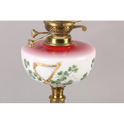 19 - A VICTORIAN BRASS OIL LAMP, the pink tinted glass reservoir painted with Gaelic harp and shamrock, o... 