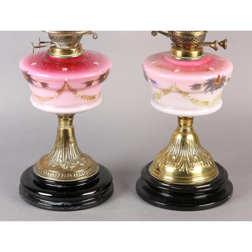 21 - A NEAR PAIR OF VICTORIAN BRASS OIL LAMPS, the pink tinted reservoirs painted with mauve flower heads... 