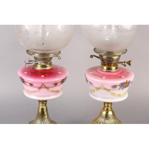 21 - A NEAR PAIR OF VICTORIAN BRASS OIL LAMPS, the pink tinted reservoirs painted with mauve flower heads... 