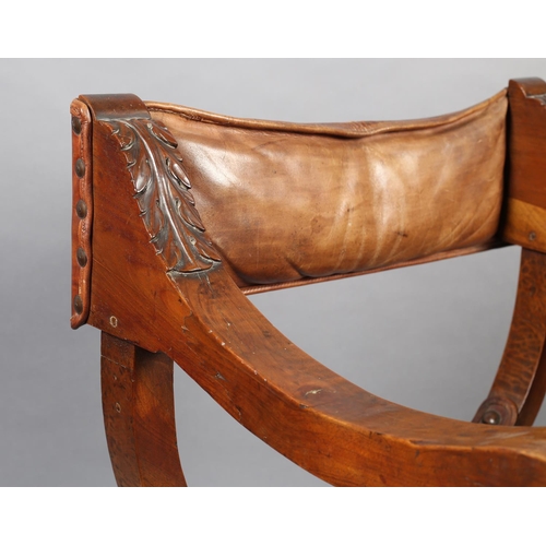 383 - A LATE 19TH CENTURY FRUITWOOD FOLDING 'X' FRAME CHAIR, having a hide sling back, leaf carved arms wi... 