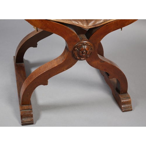 383 - A LATE 19TH CENTURY FRUITWOOD FOLDING 'X' FRAME CHAIR, having a hide sling back, leaf carved arms wi... 