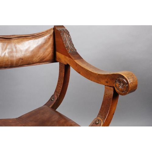 383 - A LATE 19TH CENTURY FRUITWOOD FOLDING 'X' FRAME CHAIR, having a hide sling back, leaf carved arms wi... 