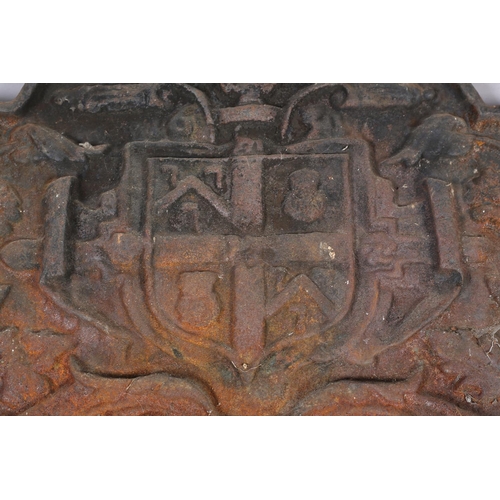 53 - A cast iron arched heraldic fireback moulded in relief with central shield flanked by trailing folia... 