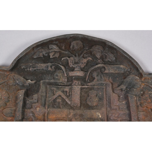 53 - A cast iron arched heraldic fireback moulded in relief with central shield flanked by trailing folia... 