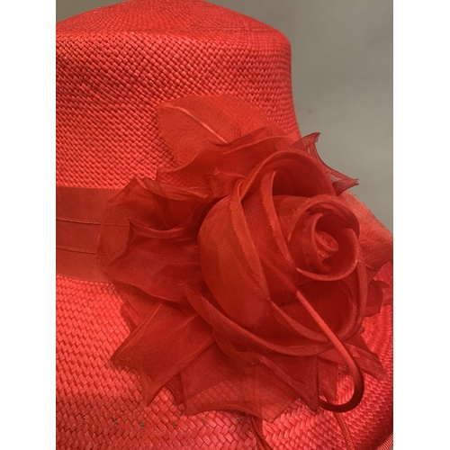 247 - Cosmo Jenks asymmetrical red straw hat with organza rose detail to the grosgrain ribbon, contained i... 