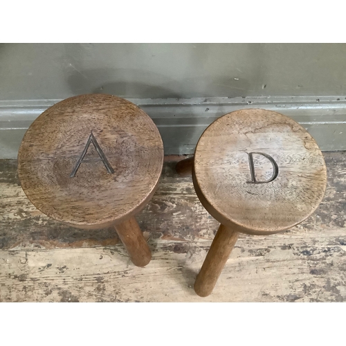 128 - A pair of two oak milking stools on three legs, the circular tops carved with A and D, 24.5cm wide