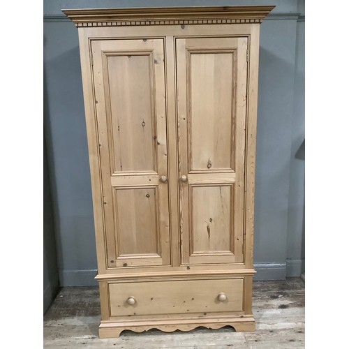 401 - A pine wardrobe having a moulded and dentil cornice above two indented panel doors with drawers belo... 