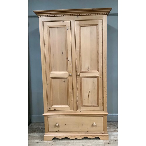 401 - A pine wardrobe having a moulded and dentil cornice above two indented panel doors with drawers belo... 