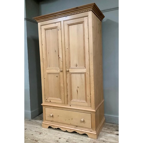 401 - A pine wardrobe having a moulded and dentil cornice above two indented panel doors with drawers belo... 