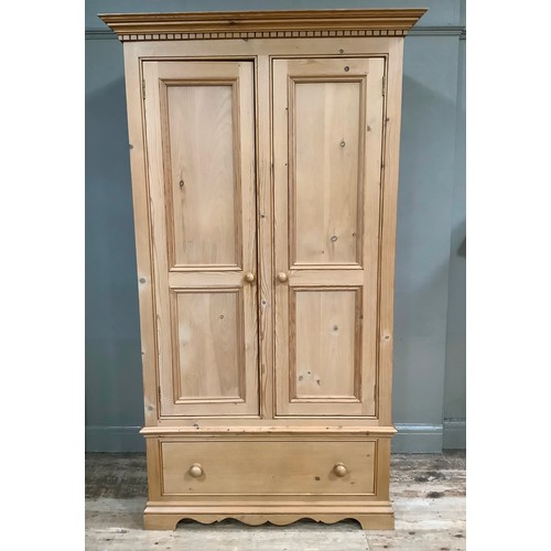 401 - A pine wardrobe having a moulded and dentil cornice above two indented panel doors with drawers belo... 