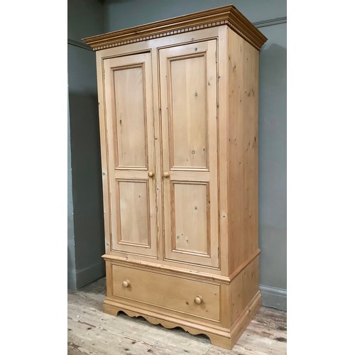 401 - A pine wardrobe having a moulded and dentil cornice above two indented panel doors with drawers belo... 