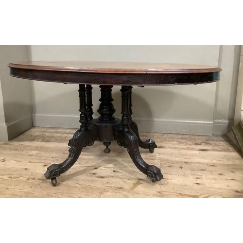 411 - A Victorian figured walnut looe table of oval outline on four column pedestal and foliate carved cab... 