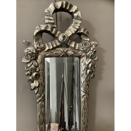 358 - A slim rectangular bevelled wall mirror in a silvered laurel leaf surround with ribboned and rose bu... 