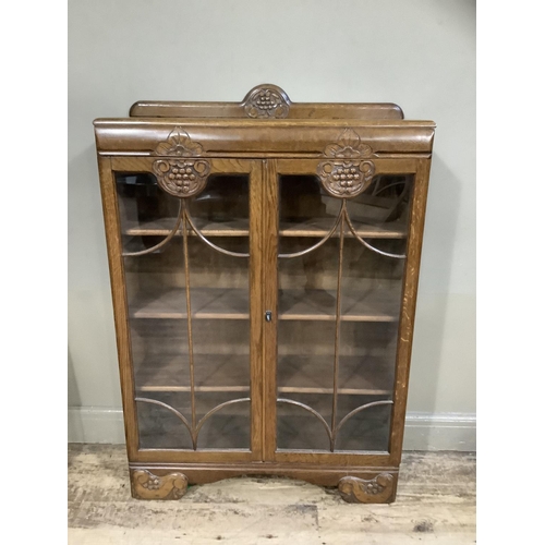 396 - A 1940s oak book case having a short raised back above two tracery glazed doors with grape vine carv... 