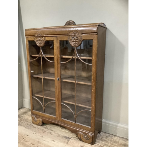 396 - A 1940s oak book case having a short raised back above two tracery glazed doors with grape vine carv... 