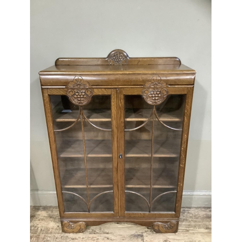 396 - A 1940s oak book case having a short raised back above two tracery glazed doors with grape vine carv... 