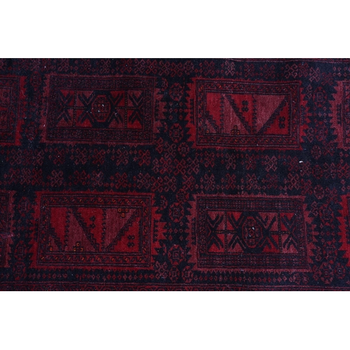 136 - An Afghan carpet, the black ground having eight deep wine rectangular panels filled with geometric d... 