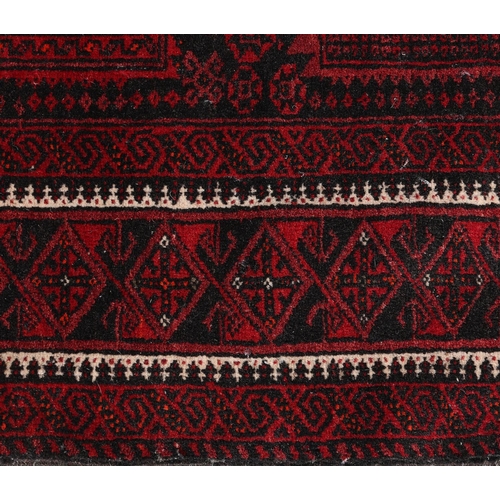 136 - An Afghan carpet, the black ground having eight deep wine rectangular panels filled with geometric d... 