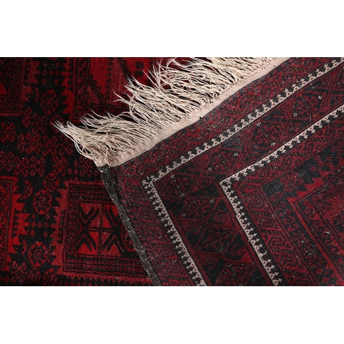 136 - An Afghan carpet, the black ground having eight deep wine rectangular panels filled with geometric d... 