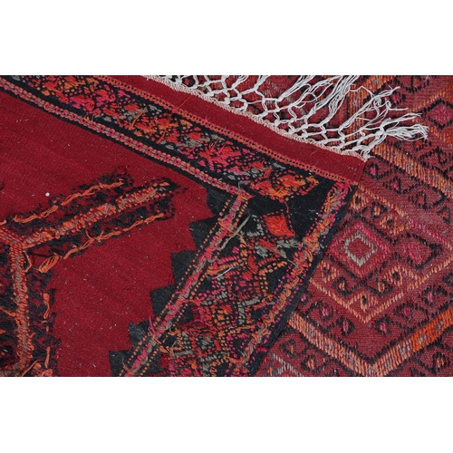 104 - A Middle Eastern carpet, the wine ground filled with a panel of multiple diamond motifs, filled with... 