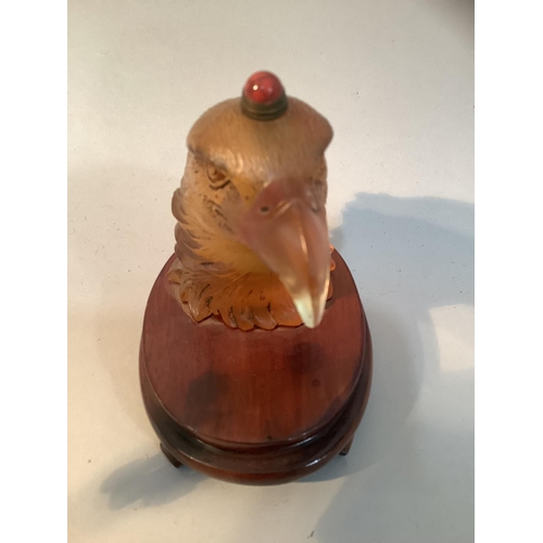 27 - A Chinese amber coloured glass eagle head snuff bottle, mounted on a stand, 11.5cm high