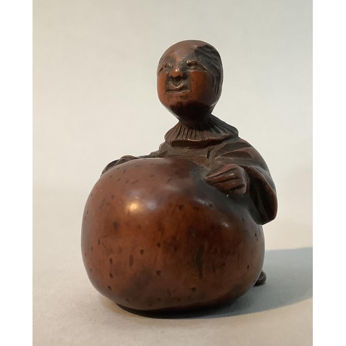 350 - A Japanese fruitwood netsuke carved as a man standing with his arms stretched around a large gourd, ... 