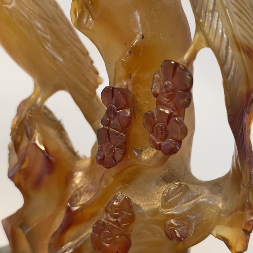 64 - A Chinese amber agate carving of birds perched on a tree stump, with hardwood stand, 16.5cm high