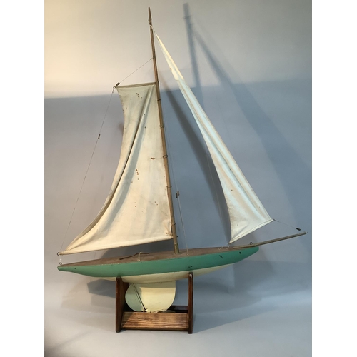 294 - A 20th century wooden model pond yacht with rigging and sails raised on a stand, painted in teal 120... 