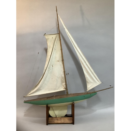 294 - A 20th century wooden model pond yacht with rigging and sails raised on a stand, painted in teal 120... 