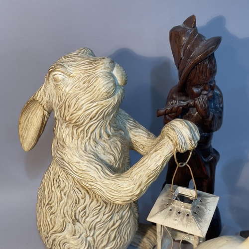 223 - A rabbit holding a lantern, model of a terrier tunnelling, wood carving of a figure playing a flute,... 