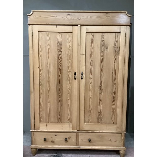 139 - A pine wardrobe with a shaped pediment, two doors above two short drawers on bun feet, 136cm wide