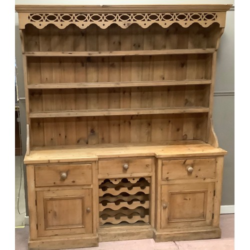 134 - A pine kitchen dresser with pierced apron frieze above a three tier plate rack above a cupboard base... 