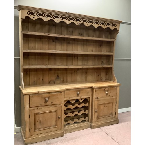 134 - A pine kitchen dresser with pierced apron frieze above a three tier plate rack above a cupboard base... 