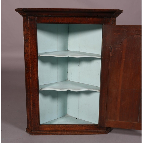 188 - AN EARLY 19TH CENTURY OAK HANGING CORNER CUPBOARD, having a moulded cornice above a single door with... 