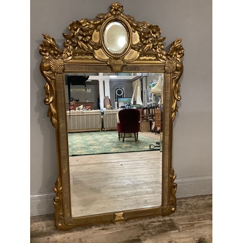 412 - A gilt composite wall mirror having bevelled glass within a frame moulded with clams, a flower pedim... 