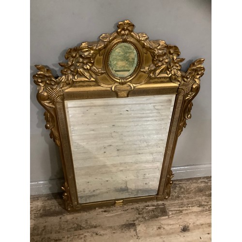 412 - A gilt composite wall mirror having bevelled glass within a frame moulded with clams, a flower pedim... 