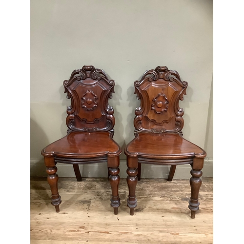 442 - A pair of Victorian mahogany heavily carved shield back hall chairs having acanthus cresting and on ... 