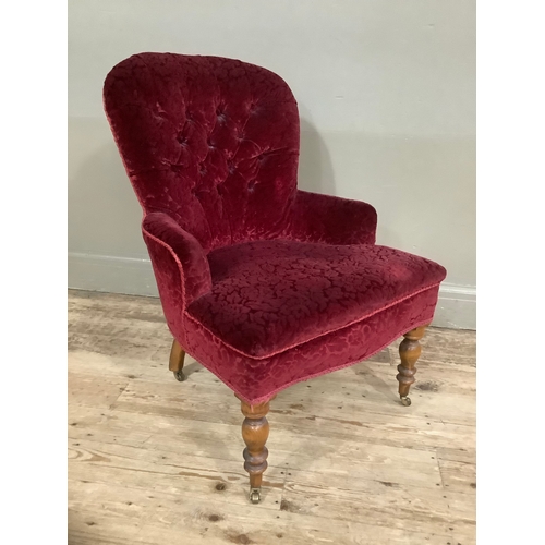 453 - A Victorian walnut button back nursing chair in red velvet fabric on turned legs with brass casters