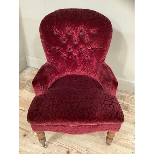 453 - A Victorian walnut button back nursing chair in red velvet fabric on turned legs with brass casters