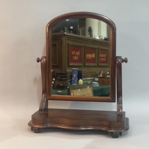 245 - A Victorian mahogany toilet mirror having an arched glass, serpentine uprights and on scrolled feet,... 