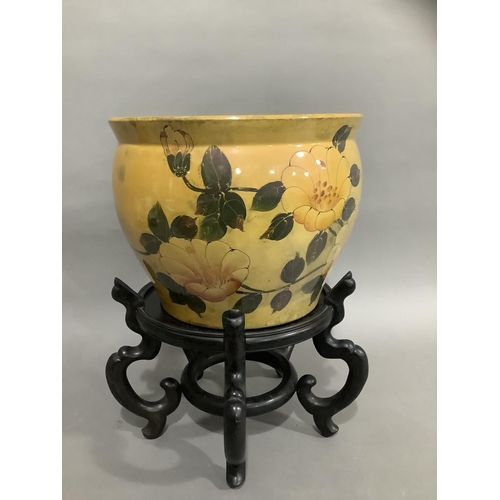 125 - A ceramic jardiniere in mustard glaze painted with flowers on carved hardwood stand, 25cm high