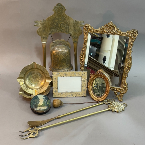 83 - A gilt metal cast table mirror, a brass bell gong, two brass engraved ashtrays, brass tongs