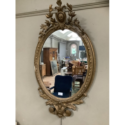 50 - A gilt ornate oval wall mirror having a shield pediment with applied foliate moulding, 95cm high