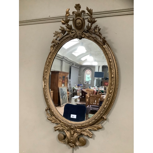 50 - A gilt ornate oval wall mirror having a shield pediment with applied foliate moulding, 95cm high