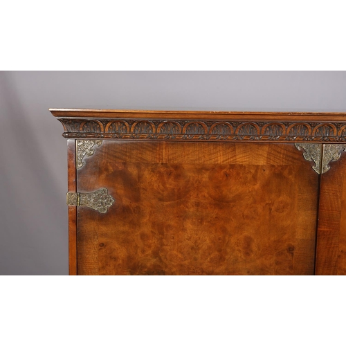 386 - A FIGURED WALNUT CROSSBANDED AND PARCEL GILT DRINKS CABINET, having a moulded cornice and demi-lune ... 