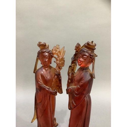 90 - A pair of Chinese carved amber effect figures of women in robes holding flowers, on carved stands, 2... 