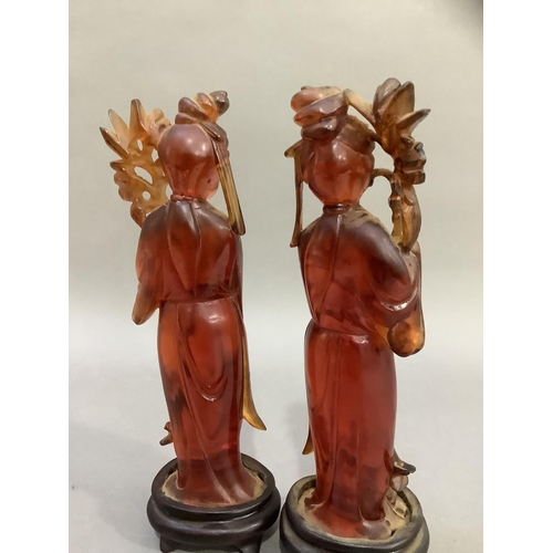 90 - A pair of Chinese carved amber effect figures of women in robes holding flowers, on carved stands, 2... 